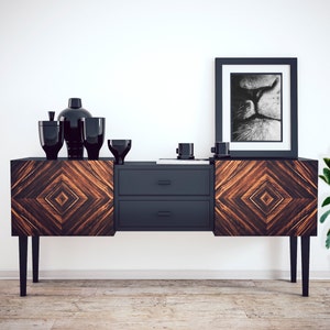 May include: A black and brown wooden sideboard with two drawers and black legs. The sideboard is decorated with a geometric pattern. There are black vases and bowls on top of the sideboard. A black and white framed print of a cat's face is hanging on the wall above the sideboard. A potted plant is on the right side of the sideboard.