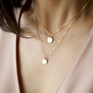 May include: A layered gold necklace with two delicate chains and two round pendant charms.