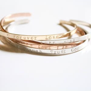 May include: Four stacked silver and rose gold bracelets with engraved messages: "Forever Love", "Luke 1:37", "Know that I am God", and "Laugh Trust God".