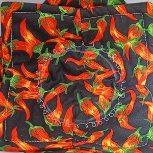 May include: Black fabric with a repeating pattern of red chili peppers. The fabric has a white stitched circle in the center.