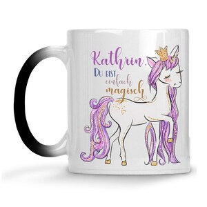 Könnte beinhalten: Weißer Keramikbecher mit einem Einhorn-Cartoon. Das Einhorn hat eine goldene Krone und eine lila-rosa Mähne. Der Becher trägt den Namen "Kathrin" und den deutschen Satz "Du bist einfach magisch".