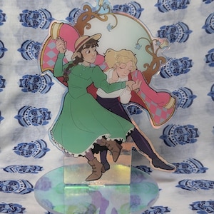 Könnte beinhalten: Ein holografischer Acryl-Ständer mit zwei Comicfiguren, einer Frau in einem grünen Kleid und einem Mann in einer roten Jacke, die zusammen tanzen. Der Ständer hat einen rosa-weiß karierten Hintergrund.