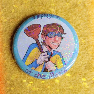 Puede incluir: Un botón redondo con una ilustración de dibujos animados de un hombre sosteniendo un desatascador. El hombre lleva gafas, un traje azul y amarillo y una corbata roja. El botón tiene el texto "Employee of the Month" en un borde azul con efecto brillante.