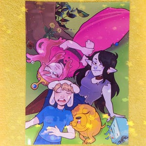May include: A vibrant illustration of characters from Adventure Time. Princess Bubblegum, Marceline, Finn, Jake, and BMO are depicted relaxing on grass beneath a tree. The artwork uses bright colours and detailed linework to bring the characters to life.