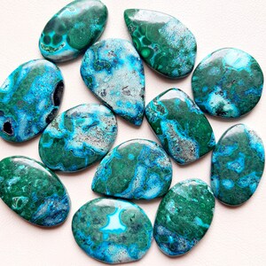 May include: A collection of 12 turquoise and green gemstone cabochons with a marbled pattern. The cabochons are teardrop shaped and have a smooth, polished finish.