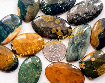 May include: A collection of polished gemstone cabochons in various oval shapes and colors, including green, brown, and yellow. A US quarter coin is included for size reference. The Etsy.com and UniversalJewels text is visible.