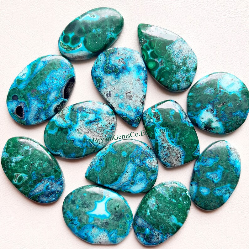 May include: Ten green and blue chrysocolla cabochons with a marbled pattern. The cabochons are oval shaped and have a smooth, polished surface.