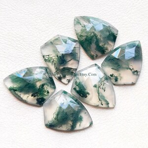 May include: Six faceted moss agate gemstones with a shield-like shape. Each stone features a translucent, milky white base with distinct, dark green, moss-like inclusions. The surfaces are polished with geometric facets. Text reads MaryamGemCo.Etsy.Com.