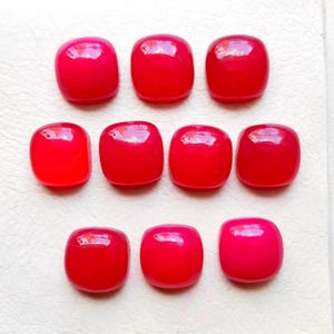 May include: Nine polished, rectangular red gemstones arranged in three rows. The stones have rounded corners and a glossy finish, reflecting light. The color varies slightly from a deep red to a lighter, brighter shade of red.