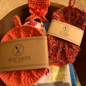 May include: A set of three kitchen items: a crocheted dishcloth, a crocheted pot scrubber, and a cotton tea towel with the text "Cause A Stir".