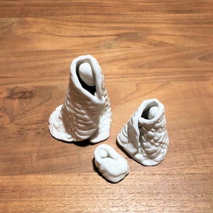 Pode incluir: Cena de natividade de cerâmica branca com três figuras: Maria, José e o menino Jesus. As figuras estão vestidas com túnicas simples e estão em pé sobre uma superfície de madeira.