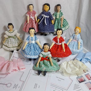 May include: Ten handmade dolls dressed in various colorful dresses and skirts. The dolls are made of wood and have painted faces. The dolls are arranged on a white surface with fabric patterns and sewing instructions.