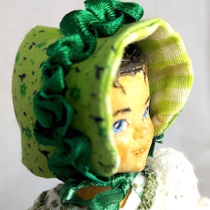 May include: A green fabric doll bonnet with a green satin ribbon and a white and green patterned fabric lining.