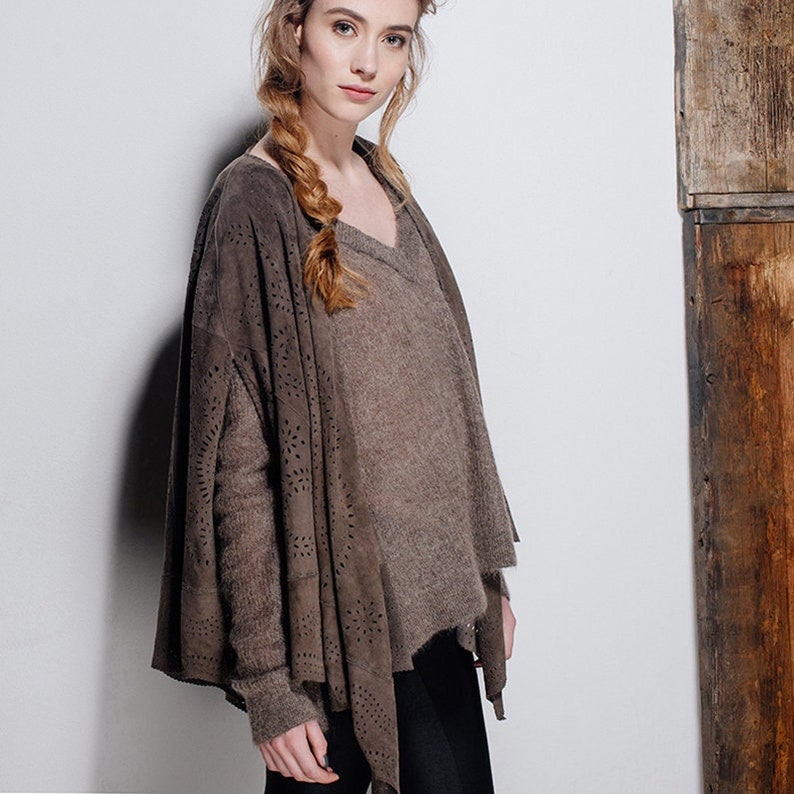 May include: A brown suede cardigan with a cut-out design. The cardigan is worn over a brown sweater and black trousers.