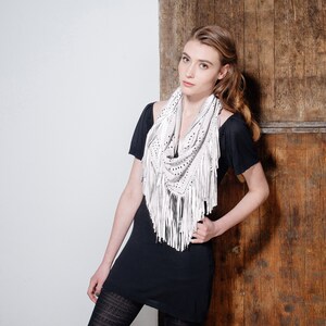 May include: A woman wearing a black dress with a white fringed scarf. The scarf has a delicate pattern and is made of leather.