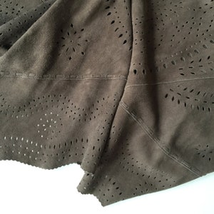 May include: Close-up of a brown suede fabric with a cut-out pattern. The fabric is folded and has a stitched seam.