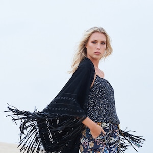 May include: A black suede fringe kimono with a beaded top and floral print trousers. The kimono has a black embroidered design and fringe trim.