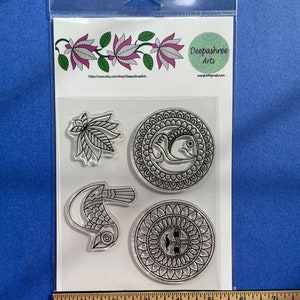 May include: A set of four clear rubber stamps with black designs. The designs include a bird, a mandala, a leaf, and a fish. The stamps are packaged in a clear plastic bag with a white label that reads "Deepashree Arts" and a website address.