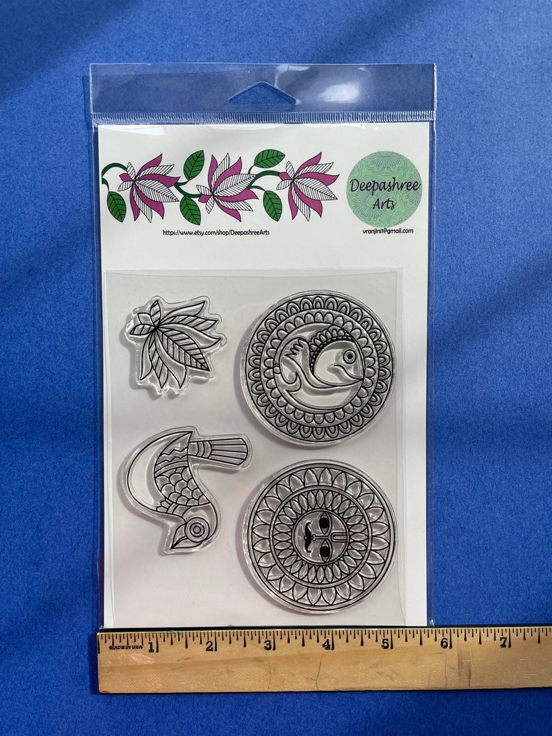 May include: A set of four clear rubber stamps with black designs. The designs include a bird, a mandala, a leaf, and a fish. The stamps are packaged in a clear plastic bag with a white label that reads "Deepashree Arts" and a website address.
