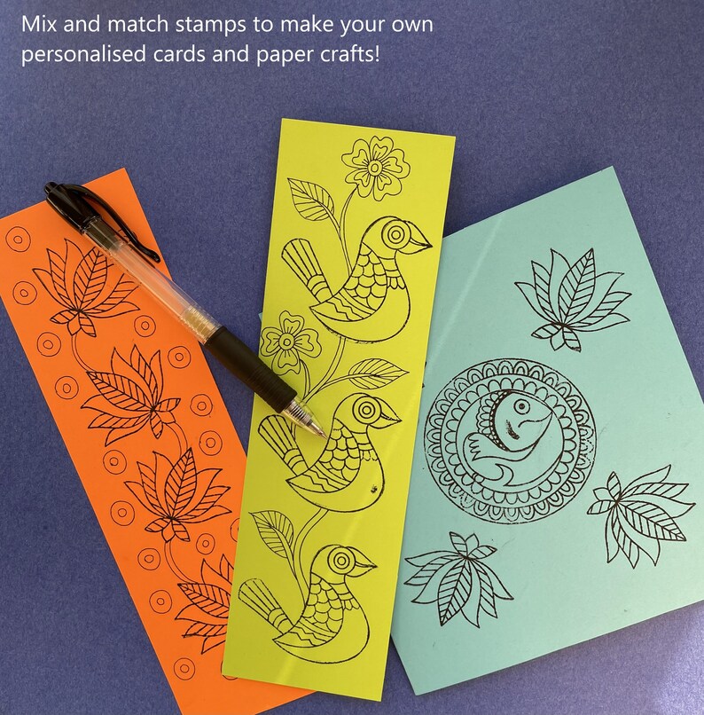 May include: Three paper craft stamps with black ink designs on a blue background. The stamps feature a bird, a lotus flower, and a fish in a circle.