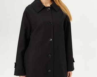 May include: A black long-sleeved coat featuring a wide collar, a front button-down closure with five visible black buttons, and straight sleeves with small tab details at the cuffs. The coat has a structured silhouette and a smooth, solid finish.
