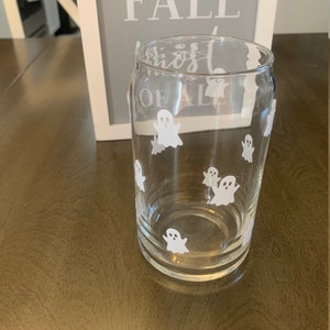 May include: A clear glass with a white ghost design. The glass is shaped like a can and has a rounded bottom.