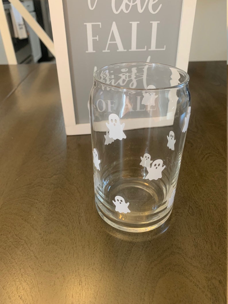 May include: A clear glass with a white ghost design. The glass is shaped like a can and has a rounded bottom.