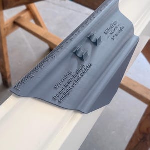May include: A grey plastic MiterPro 5" baseboard miter tool with an integrated ruler along the edge. The tool features two small raised guides and embossed text that reads: "Warning Do not leave in direct sunlight or hot vehicles" and "MiterPro TOOLS 5" base".