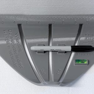 May include: A gray MiterPro Tools miter guide featuring a built-in level, a ruler along the top edge, and slots for angle marking. A black permanent marker is held in the center. Text on the tool reads: Warning Do not leave in direct sunlight.