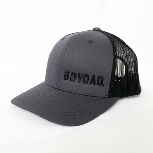 May include: A gray and black trucker hat with the text "BOYDAD." embroidered in black on the front.