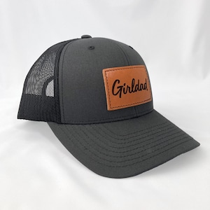 May include: Black trucker hat with a brown leather patch that says "Girldad" in brown script.