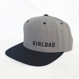 May include: A gray and black baseball cap with the word "GIRLDAD" embroidered in black on the front.