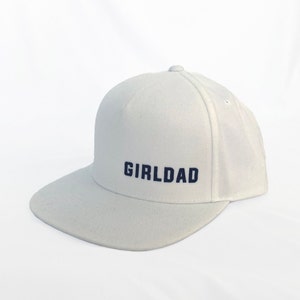 May include: White baseball cap with a navy blue embroidered text that reads "GIRLDAD".
