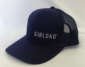 May include: Navy blue baseball cap with a mesh back and curved brim. The cap features the embroidered text "GIRLDAD" in a light gray color. The hat is a classic trucker style.