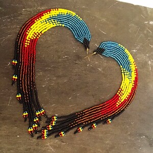 May include: A pair of long, beaded earrings with a gradient of red, yellow, blue, and black beads. The earrings are shaped like a curved line and have a fringe of beads at the bottom.