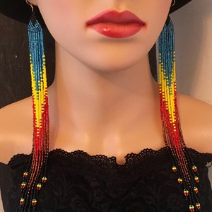 May include: Long beaded earrings with a gradient of red, yellow, blue, and black beads. The earrings are hanging from a person's ears.