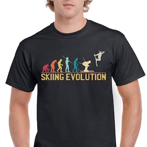 Könnte beinhalten: Ein schwarzes T-Shirt mit einer Grafik im Vintage-Stil, die die Evolution des Skifahrens zeigt. Die Grafik zeigt eine Reihe von Strichmännchen, die sich von einem Höhlenmenschen zu einem modernen Skifahrer entwickeln. Der Text "Skiing Evolution" ist unter der Grafik gedruckt.