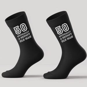 May include: A pair of black socks with the number "50" and the text "OFFICIALLY A GRUMPY OLD MAN" printed in white. The socks are made of a soft material and are designed to fit the foot and ankle.