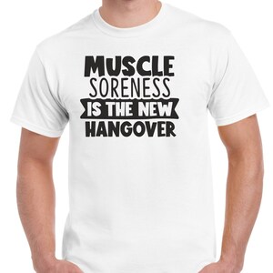 May include: White t-shirt with black text that reads "Muscle Soreness Is The New Hangover".