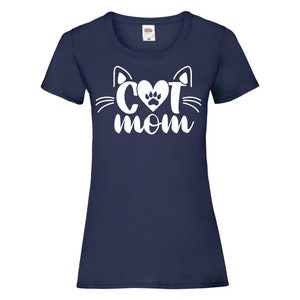 Peut inclure: Un t-shirt bleu marine avec un motif blanc repr&eacute;sentant un visage de chat avec un c&oelig;ur et une empreinte de patte au milieu et le texte "CAT MOM" en dessous.