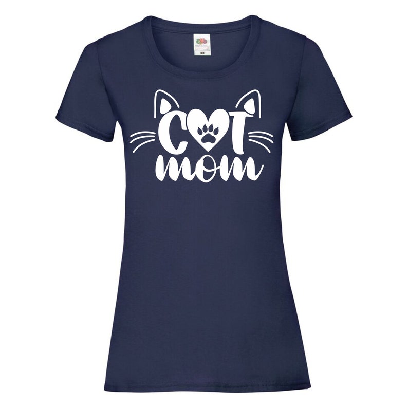 Peut inclure: Un t-shirt bleu marine avec un motif blanc repr&eacute;sentant un visage de chat avec un c&oelig;ur et une empreinte de patte au milieu et le texte "CAT MOM" en dessous.