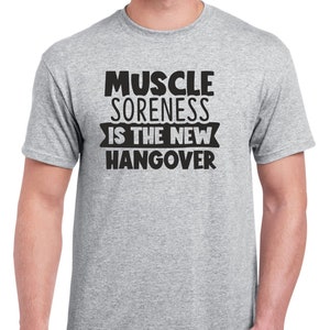 May include: A heather grey t-shirt with black text that reads "Muscle Soreness Is The New Hangover".