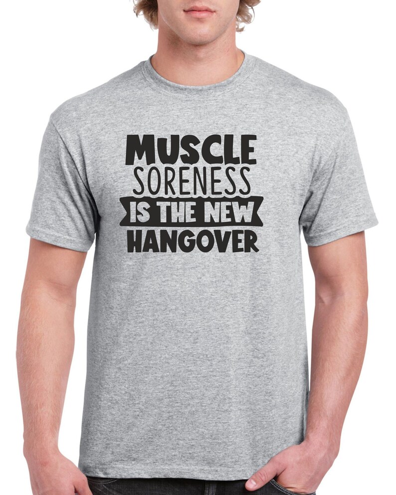 May include: A heather grey t-shirt with black text that reads "Muscle Soreness Is The New Hangover".