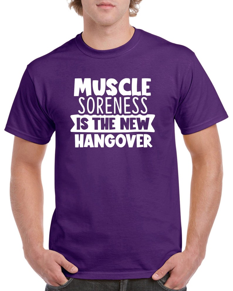 May include: Purple t-shirt with white text that reads "Muscle Soreness Is The New Hangover".