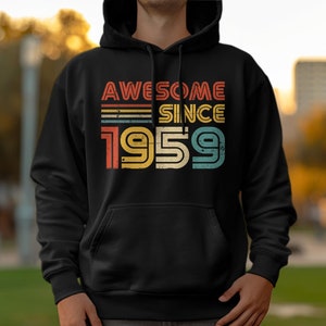 以下が含まれることがあります： 「Awesome Since 1959」というヴィンテージスタイルのグラフィックがプリントされた黒いフード付きスウェットシャツです。