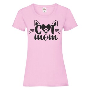 Peut inclure: T-shirt rose avec un motif noir repr&eacute;sentant un visage de chat avec un c&oelig;ur et une empreinte de patte au milieu et le texte "Cat Mom" en dessous.