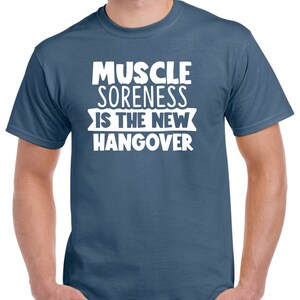 May include: A blue t-shirt with white text that reads "Muscle Soreness Is The New Hangover".