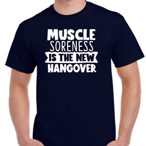 May include: A navy blue t-shirt with white text that reads "Muscle Soreness Is The New Hangover".