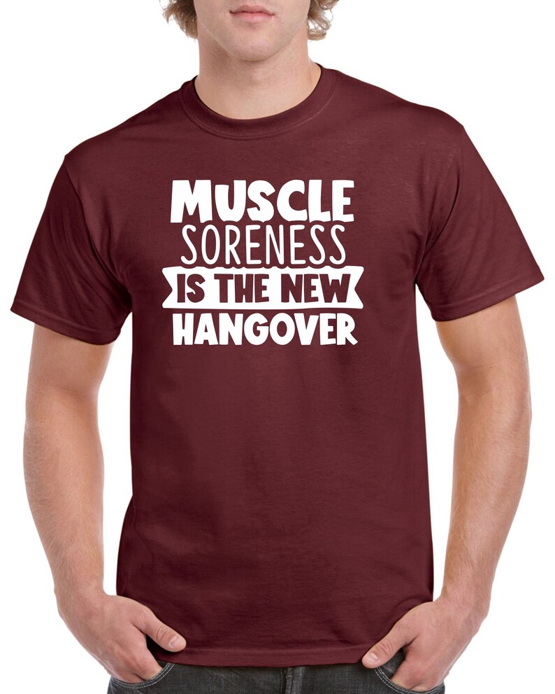 May include: A maroon t-shirt with white text that reads "Muscle Soreness Is The New Hangover".