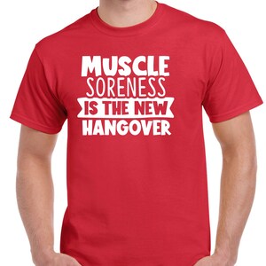 May include: Red t-shirt with white text that reads "Muscle Soreness Is The New Hangover".
